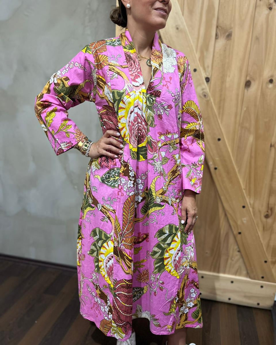 Woman wearing a vibrant pink dress with floral and leaf patterns against a wooden wall.