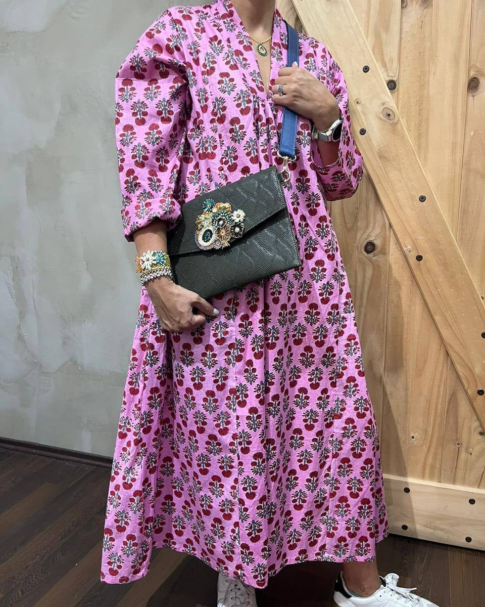 Person wearing a pink floral dress holding a black clutch against a wooden and concrete wall.